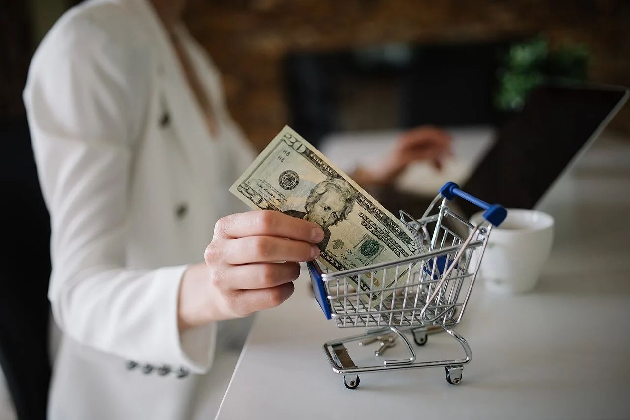 Donna che fa acquisti online dal computer con un piccolo carrello sulla scrivania