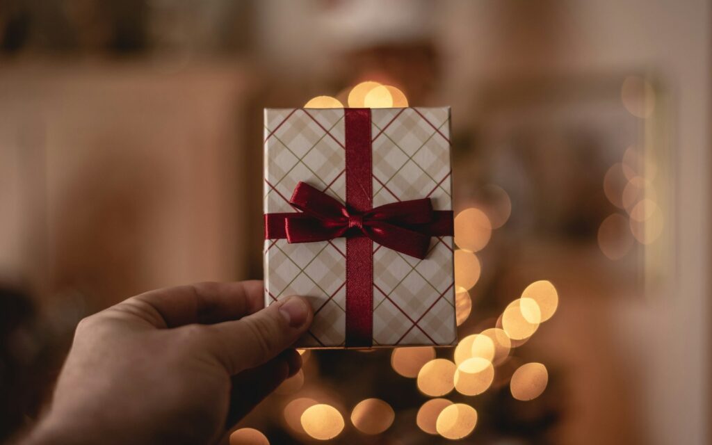 Mano che tiene una piccola confezione regalo con fiocco rosso tra luci natalizie