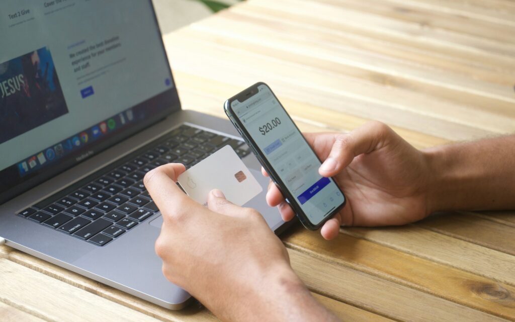 Mani con smartphone e carta di credito accanto a un laptop per confermare un pagamento